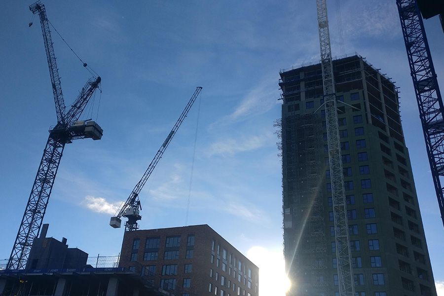 Image showing tops of buildings under construction, with several cranes in place bulding sites that use heat networks. Behind the constructions is blue sky with the sun shining.